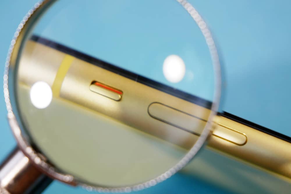Detalle del lateral de un teléfono móvil bajo una lupa, representando la sospecha de que el teléfono escucha nuestras conversaciones para mostrar anuncios de lo que hablas.